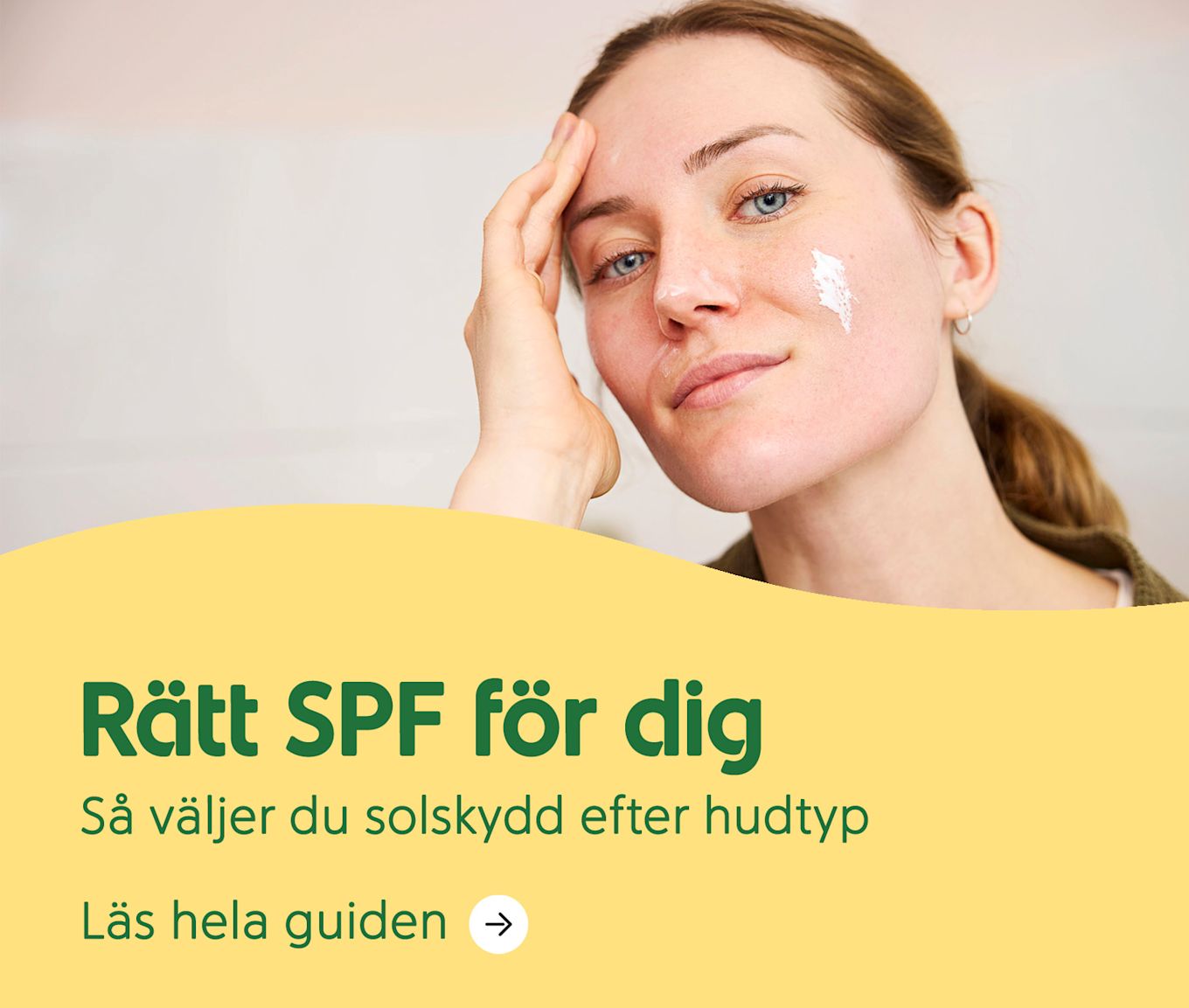 Kvinna applicerar solkräm på kinden med handen mot pannan i en ljus inomhusmiljö. Text: Rätt SPF för dig. Så väljer du solskydd efter hudtyp.