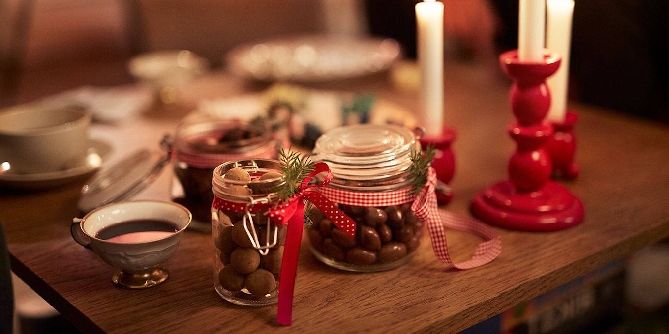 Bord med uppdukat adventsfika, tända ljus och glasburkar med julig choklad.