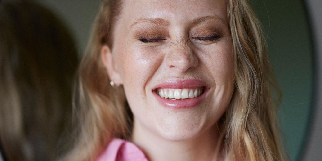 Sminkad kvinna ler och kniper ihop ögonen.