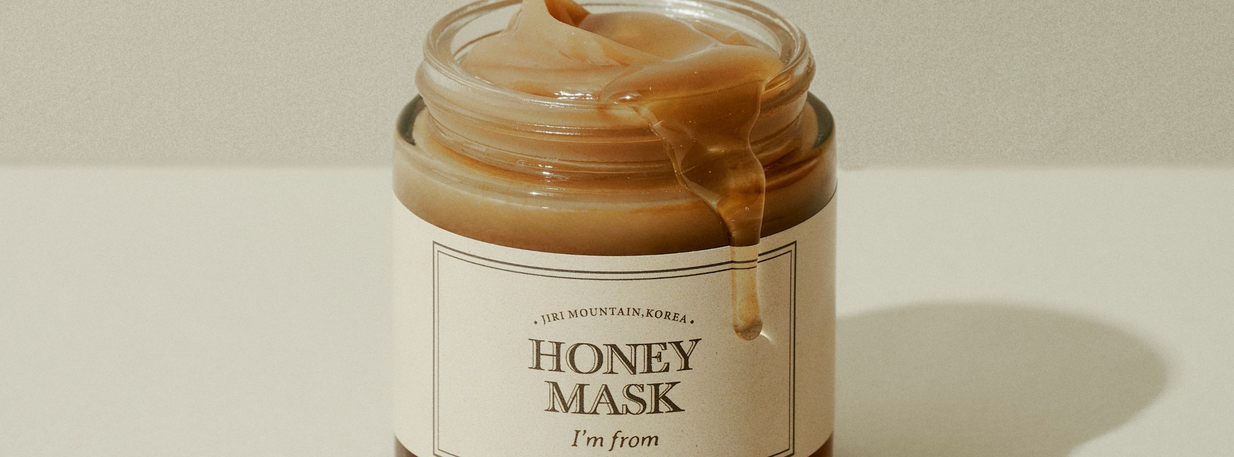 Burk med ansiktsmask märkt "Honey Mask" från "I'm from", honung rinner ner längs kanten på burken mot en ljus bakgrund.