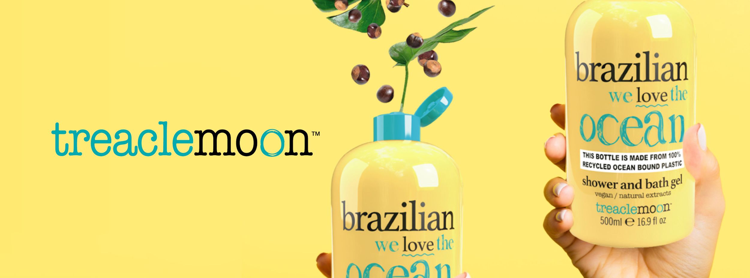 Hand håller en gul flaska Treaclemoon dusch- och badgel "Brazilian we love the ocean" mot gul bakgrund, med gröna blad och bär ovanpå flaskan.