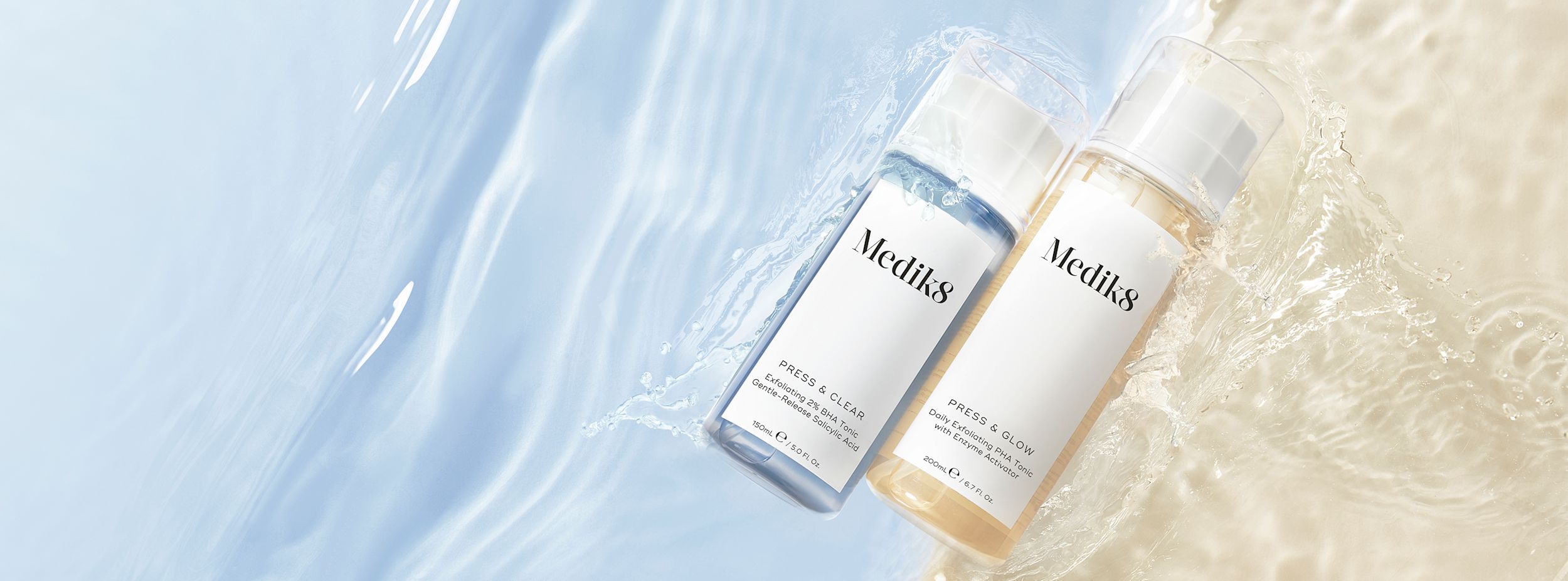 Två flaskor Medik8 ansiktsvatten, en blå och en gul, ligger på en våt yta med vattenstänk och ljus bakgrund.