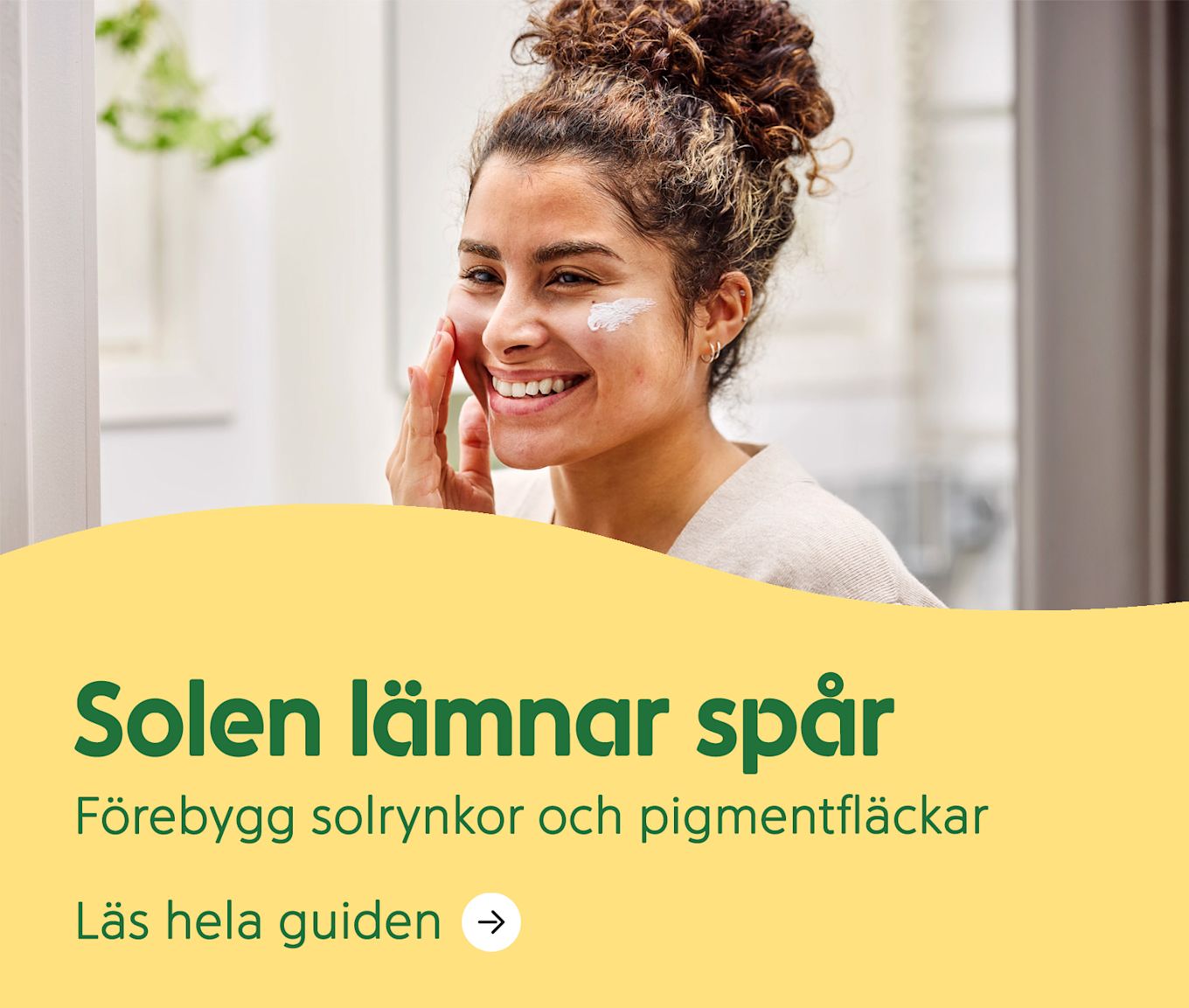 Kvinna ler och applicerar solkräm på kinden framför en spegel i ett ljust rum. Text: Solen lämnar spår. Förebygg solrynkor och pigmentfläckar.