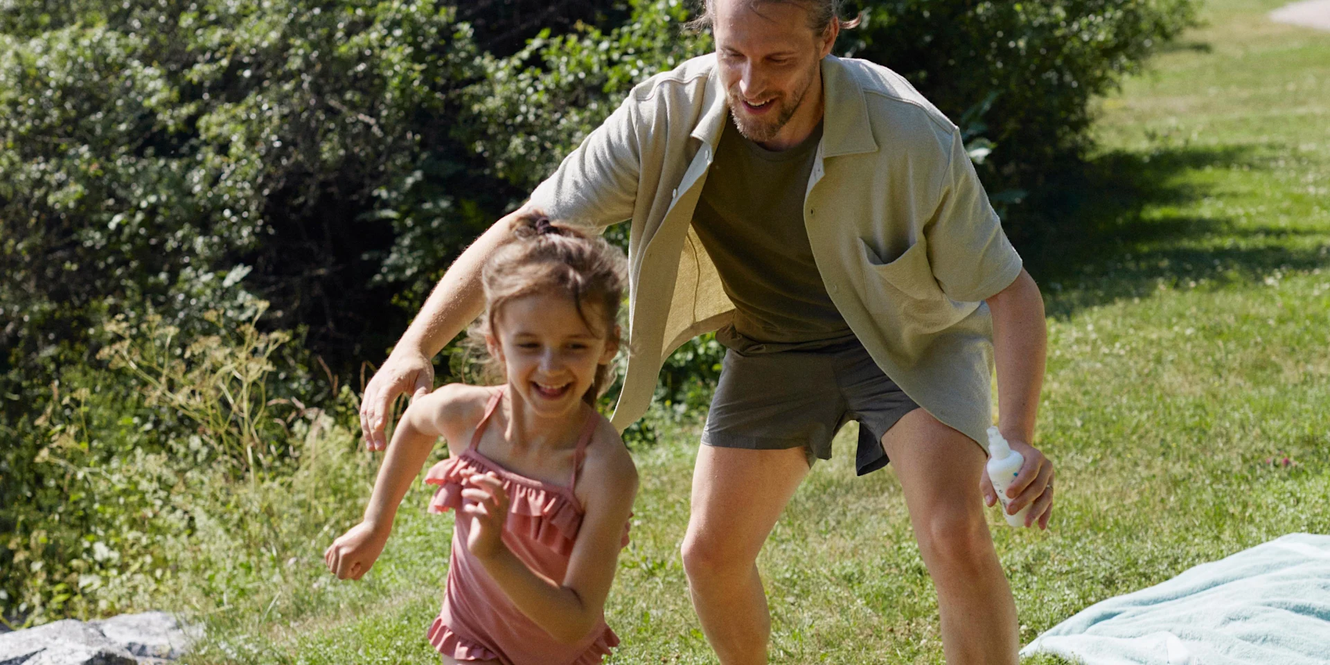 Pappa och dotter leker utomhus i solskenet.