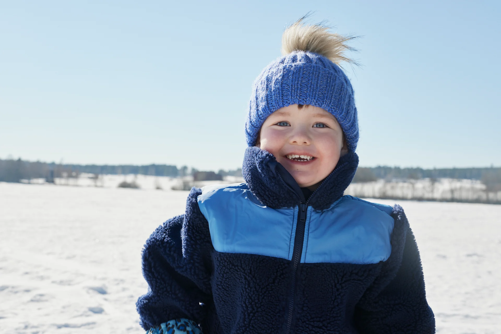 Pojke leker ute i snön, iklädd blå jacka och blå mössa.