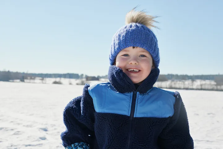 Pojke leker ute i snön, iklädd blå jacka och blå mössa.