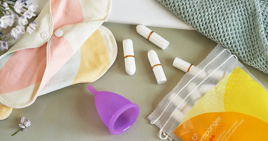 På ett bord ligger en påse med tamponger från Apotek Hjärtat, en menskopp och en tygbinda.