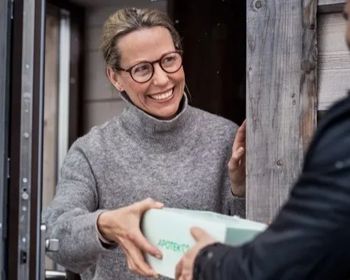 Kvinna står i dörröppningen och tar emot ett paket som hon har beställt med hemleverans.