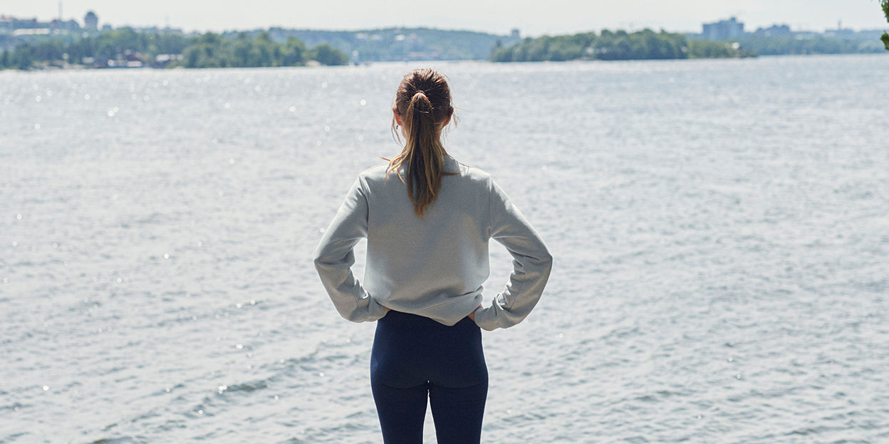 Kvinna i träningskläder står och ser ut över vattnet en solig och varm dag. 