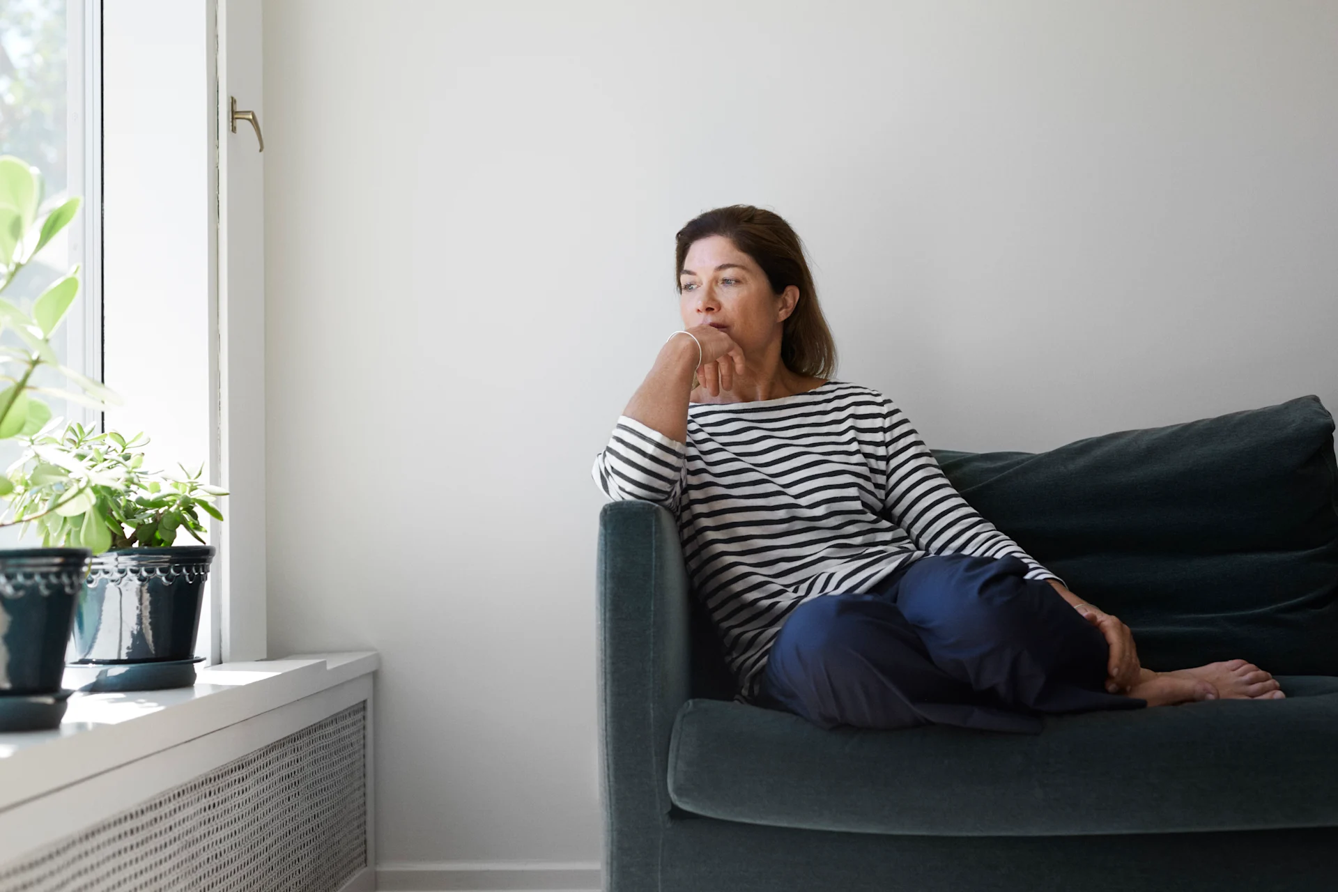 Kvinna sitter i soffa och tittar ut genom fönstret.