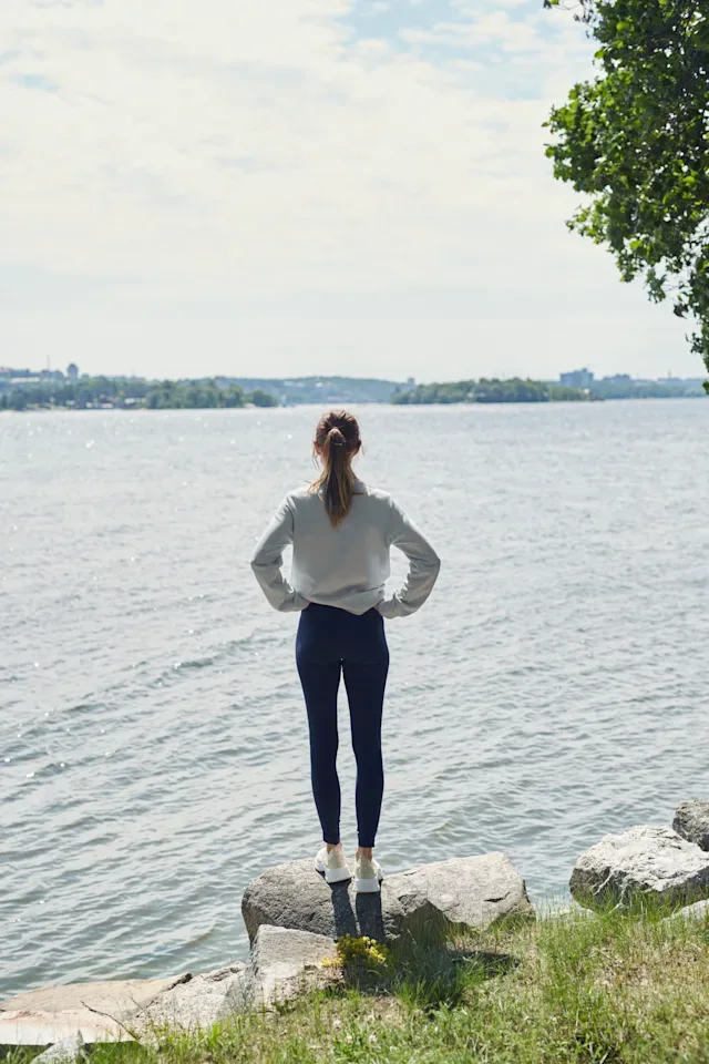 En kvinna står på en sten vid vattnet och tittar ut mot skärgårdsöar i horisonten.