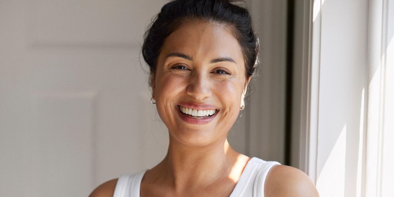 Kvinna står i badrum och ler, solen lyser in genom fönstret.