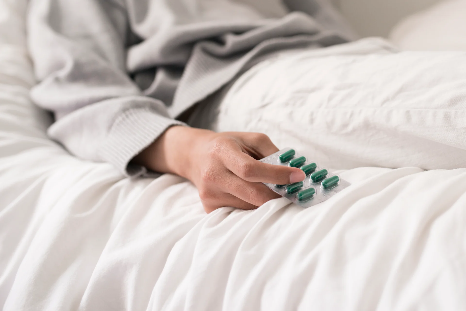 En person ligger nedbäddad i sängen och håller en pillerkarta i handen.