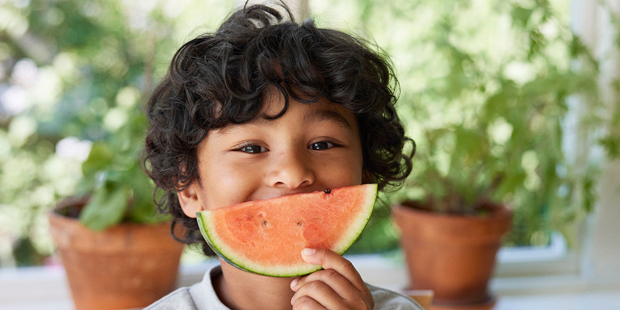 Barn håller upp en vattenmelon framför munnen som är format till ett leende.