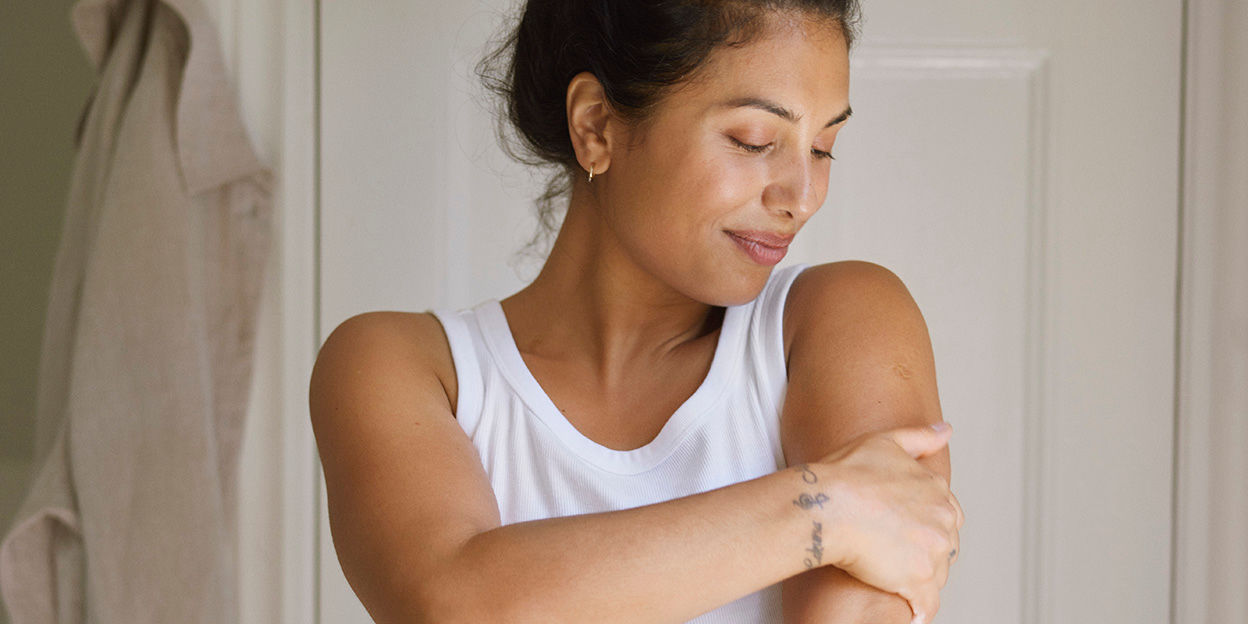 Kvinna iklädd linne smörjer in sin ena arm.