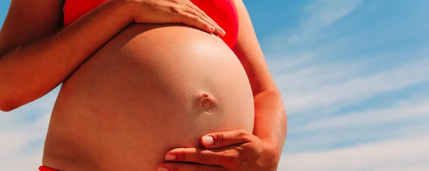 En närbild av en gravid kvinnas mage mot en klarblå himmel.