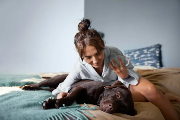 Kvinna ligger och kramar sin hund i sängen.
