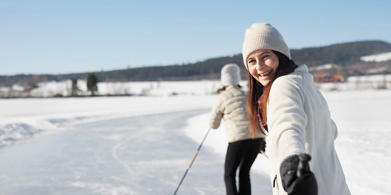 Glad kvinna åker långfärdsskridskor i ett vackert vinterlandskap.