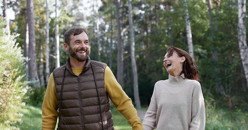 Man och kvinna håller hand när de går i skogen. Båda skrattar och ser glada ut.