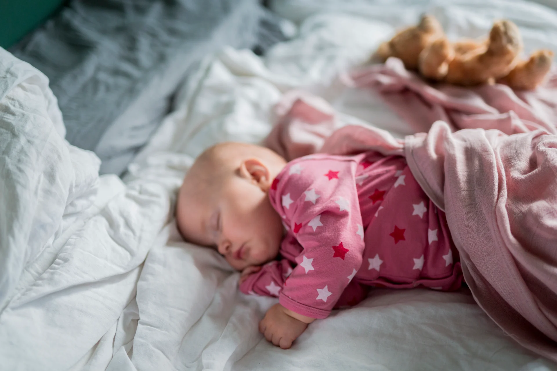 Bebis ligger och sover i en säng, iklädd en rosa sparkdräkt med stjärnor på.
