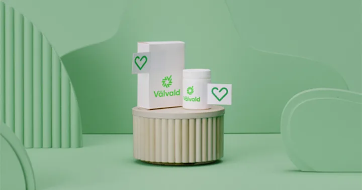 På en cylinder i trä står två vita förpackningar märkta med Apotek Hjärtats symbol, en ask och en burk. Tryckt på förpackningarna står det med grönt ordet välvald och dess symbol.