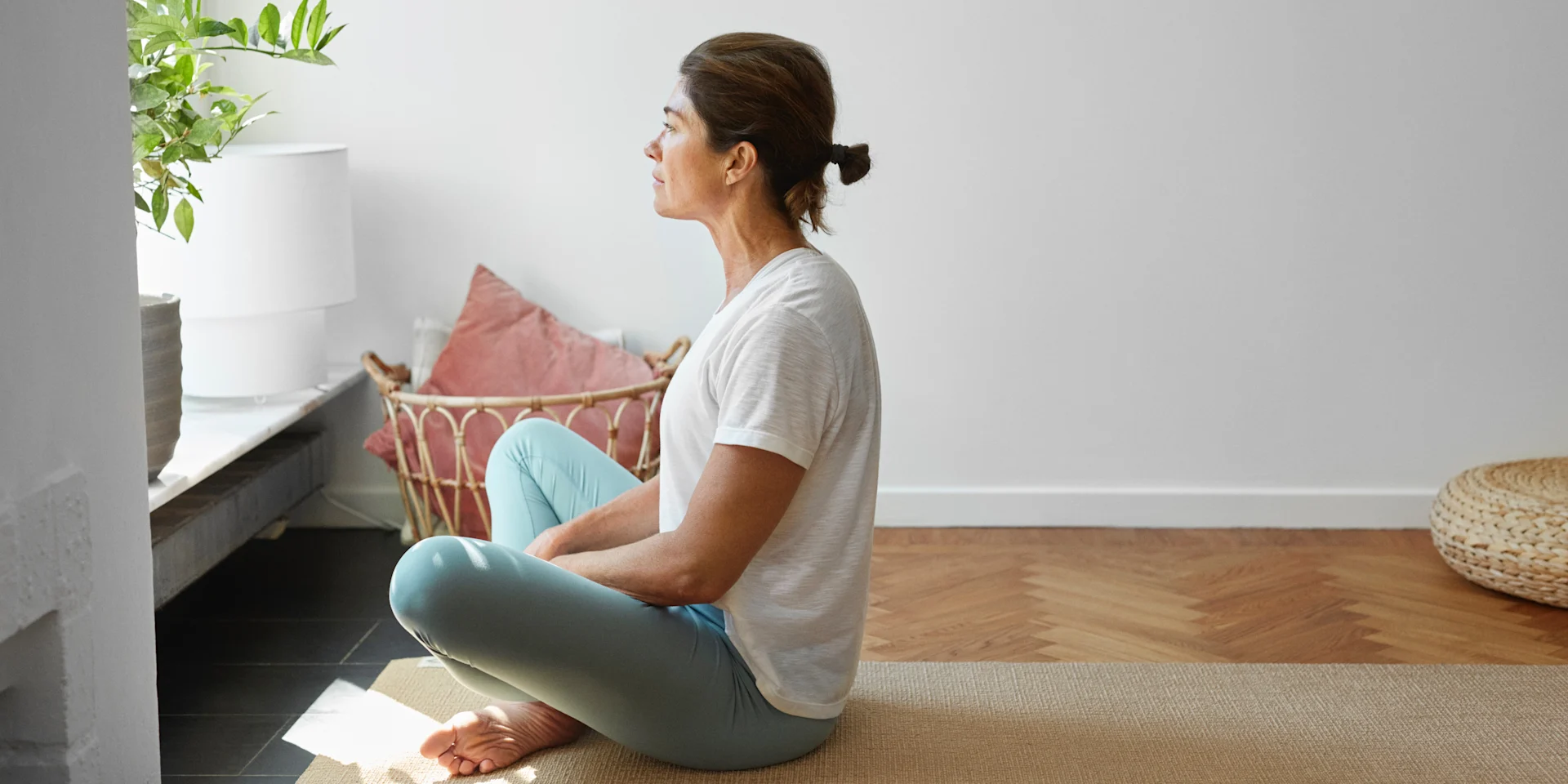 Kvinna sitter på en yogamatta och tittar ut genom fönstret.