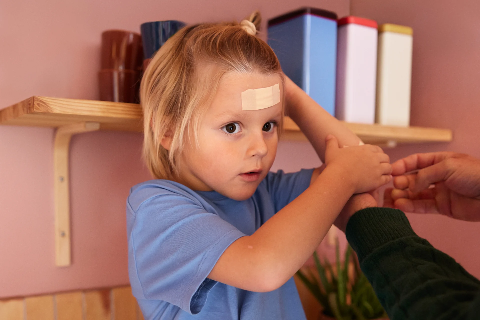 Son har fått ett stort plåster i pannan av sin mamma, sitter på en köksbänk.
